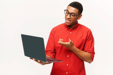 Kırmızı tişörtlü, beyaz dizüstü bilgisayar kullanan gülümseyen yakışıklı Afro-Amerikan genç adam. Dost canlısı, çok kültürlü bir öğrenci, gözlüklü serbest çalışan, uzaktan kumanda için bilgisayar kullanan.