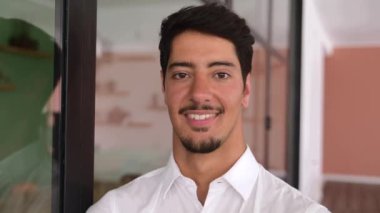 Cheerful and serene latin businessman in formal white shirt, headshot of young handsome guy, male white collar worker looks at the camera with toothy smile
