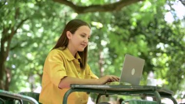 Açık havada dizüstü bilgisayar kullanan neşeli kadın serbest yazar. Yazlık kafede masa başında oturmaktan keyif alıyor. Parkta dizüstü bilgisayar kullanan gülümseyen bir kadın.