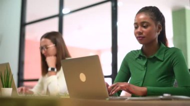 People working in coworking space. Focused African-american female employee using laptop computer on the foreground