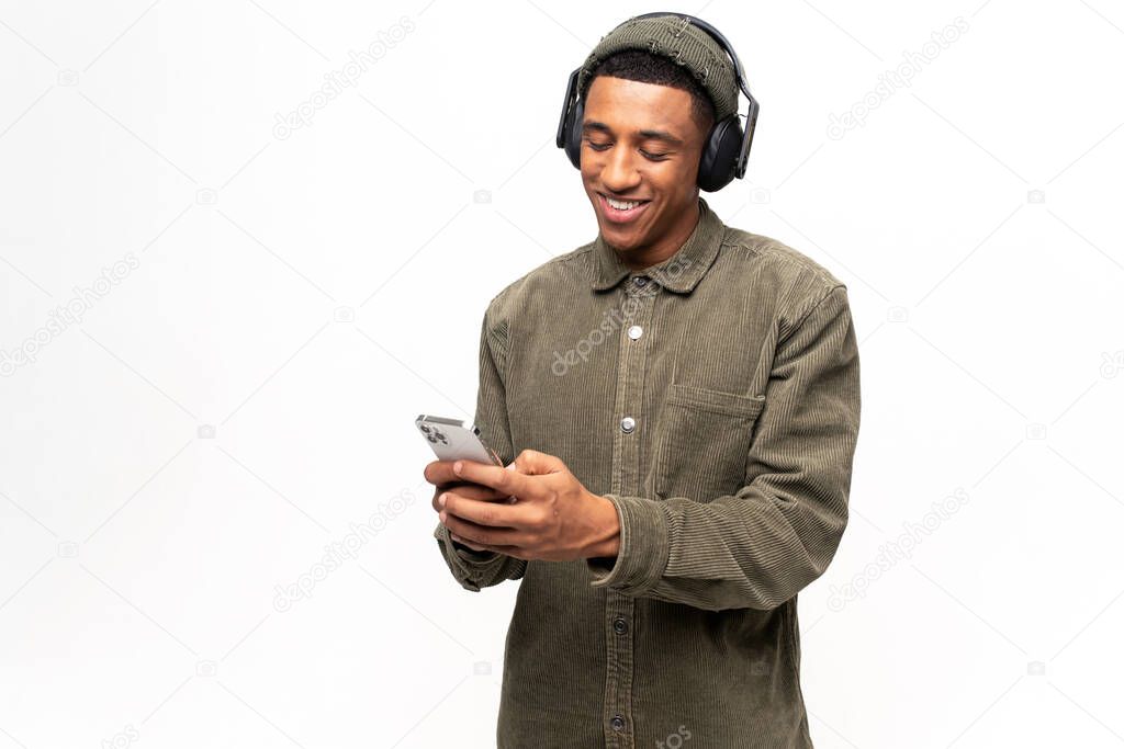 Hilarious multiracial man wearing headphones using a smartphone, spends leisure online, watching videos, listening music and smiles, happy guy with earphones holds phone, isolated on white