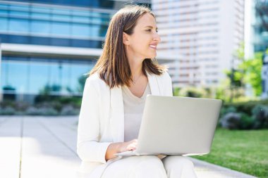 Gündelik kıyafetlerle gezen kadın ofis çalışanı dışarıda oturan dizüstü bilgisayarı kullanan, şehirde oturan, daktilo yazan, e-postalarına cevap veren genç ve çekici bir kadın.