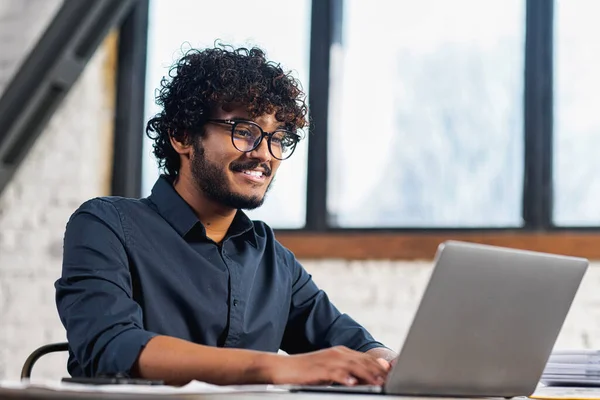 Low angle view of the concentrated man looking at the laptop screen with happy expression while looking from the office. Smart guy at work concept