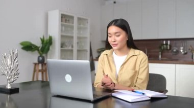 Zeki Asyalı bayan yönetici ofis masasında oturuyor, dizüstü bilgisayara el sallıyor, çok ırklı kadın müşteriyle çevrimiçi konuşuyor, müşteriyle projeyi tartışıyor, online iş görüşmesi yapıyor.