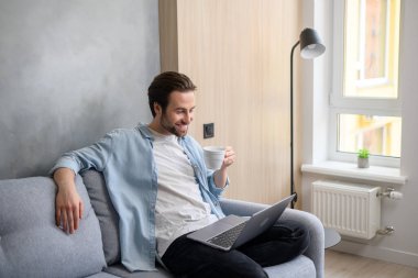 Rahat ev atmosferinde dizüstü bilgisayar kullanan, kanepede oturup daktilo kullanan, internette sörf yapan, film izleyen 30 'lu yaşlardaki dingin beyaz bir adam. Kaygısız adam içecek içiyor.