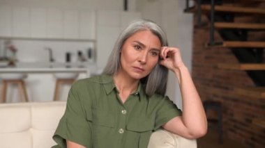 Depresyon kavramı. Üzgün, yaşlı, gri saçlı, Asyalı bir kadının evdeki kanepede oturup düşüncelere ve endişelere dalmış, kuşkulu bir kadın gibi ağır bir umutsuzluk ve üzüntü duygusu vardır.