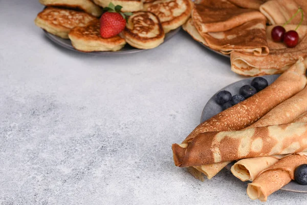 Old-fashioned fluffy pancakes and crepe with berries on grey background. Variety of pancakes. Thin and fluffy pancakes with blueberries, strawberry and sweet cherry.