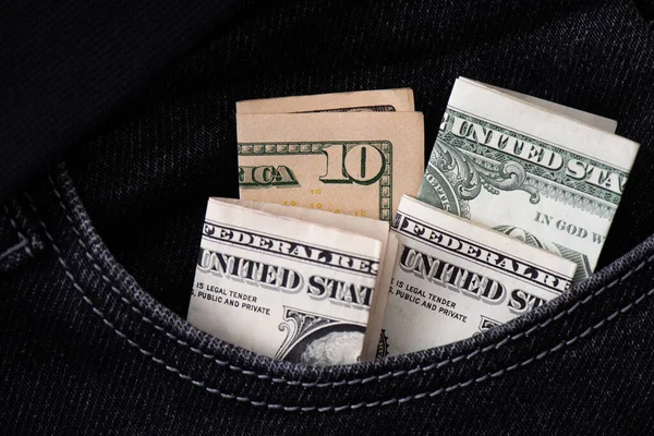 Four folded US dollar banknotes stick out in the pocket of black jeans. Saving, storing and exchanging money business background. American money in denominations of a dollar and a ten close up.