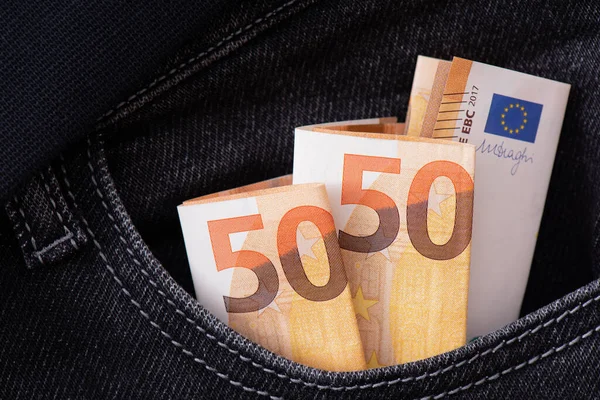 Three folded fifty euro notes protrude from the pocket of black jeans. Financial background. Savings and storage of money concert. Paper banknotes of Euros denominations of fifty euros close-up