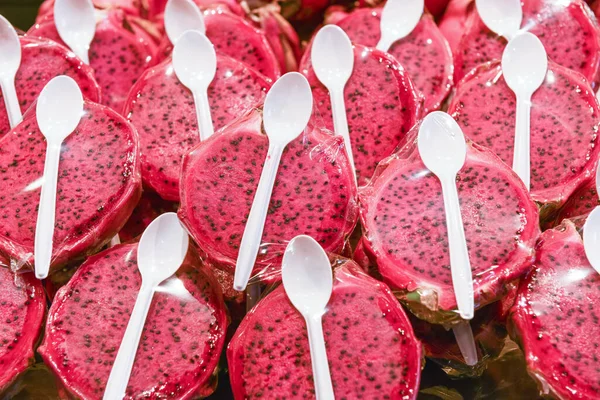 Red pitahaya packed in stretch film with plastic spoons. Exotic dragon fruits lies on counter in grocery store for sale close view