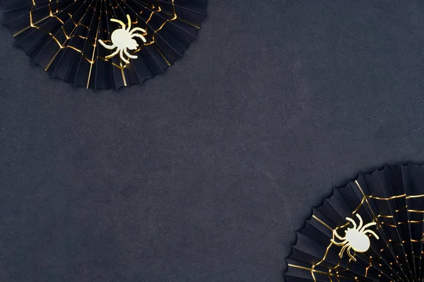 Golden spider and cobweb on a dark background. Scary Halloween shiny spiders and black paper fans with golden cobwebs. Halloween decorations on a black textured backdrop with copy space.