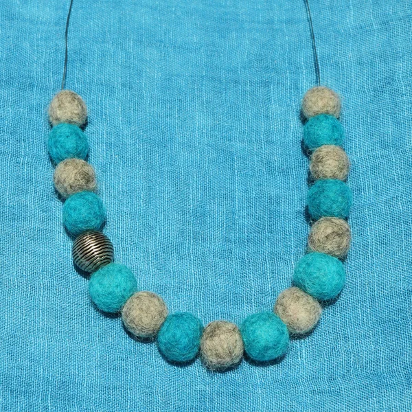 Felt and metal necklace on turquoise linen background — Stock Photo, Image