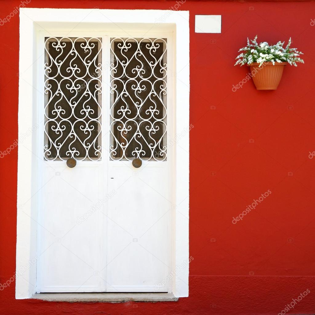 ornamental white double door and vivid red wall with hanging fl