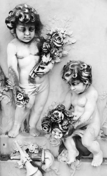 Zwei kleine Engel mit Blumen - Relief auf Grab auf monumentalem Stein Stockbild