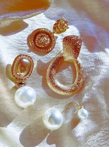 Background of accessories. A set of beautiful precious jewelry made of gold and pearls on a silk scarf. Fashion photos