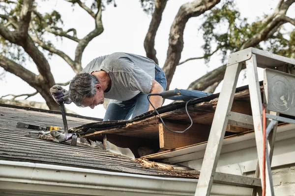 Muž zkoumání a opravit děravou střechu domu — Stock fotografie