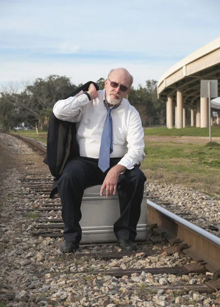 Tired Jobless senior businessman sits on suitcase on railroad train tracks