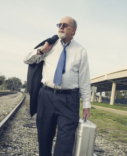 Angry, jobless senior businessman walking along railroad train tracks — Stock Photo, Image