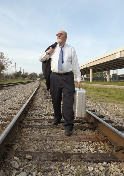 Angry, jobless senior businessman walking along railroad train tracks — Stock Photo, Image