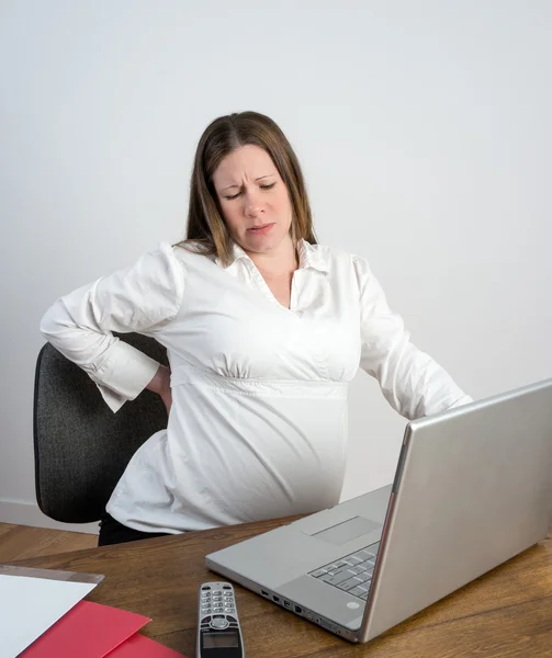 Zwangere vrouw haar pijnlijke rug zitten aan een bureau uitrekken — Stockfoto