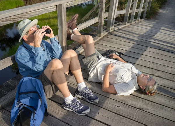 Seniors birdwatching and relaxing on old wooden foot bridge — Stock Photo, Image