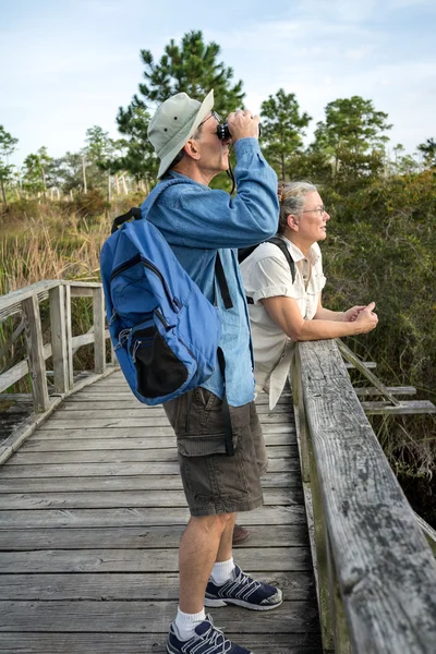 Starší pár turistiku a pozorování ptactva na stará dřevěná lávka — Stock fotografie