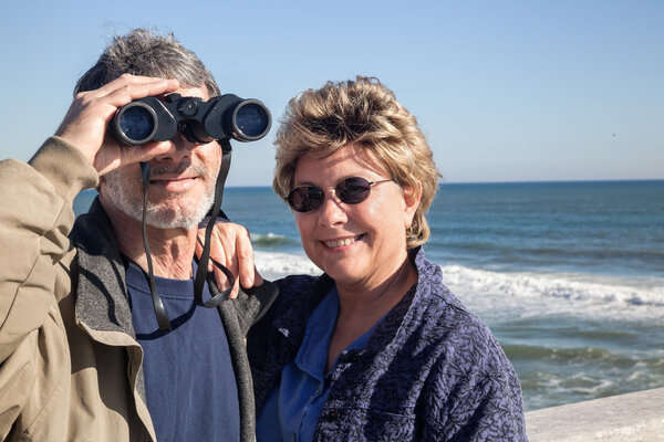 Retired couple on beach vacation birdwatching with binoculars