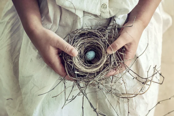 Fille tenant l'oeuf moucheté bleu dans le nid d'oiseau sur le tour — Photo