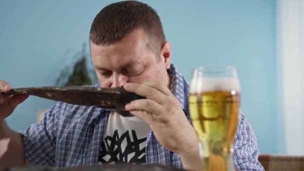 Ung man med fisk i händerna njuter av doften av läckra färska skaldjur och öl i ett glas samtidigt som du kopplar av hemma — Stockvideo