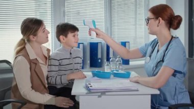 Tıp doktoru ve hastaların portresi, terapist temas olmayan termometresi olan çocuğun sıcaklığını ölçer ve sağlık kliniğindeki aşıdan bahseder.