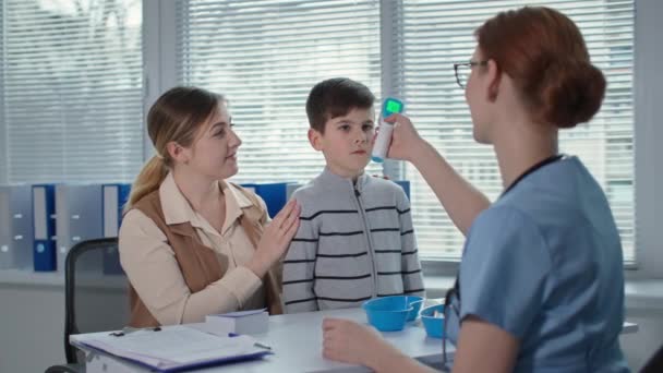 Klinika zdrowia, lekarz mierzy temperaturę chłopca z bezdotykowym termometrem i pokazuje lek w szklanej butelce — Wideo stockowe