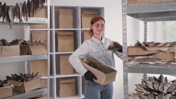 Small business, charming woman in gloves takes large sea salt fish from shelf and puts it in box while working in fish warehouse — Stock Video