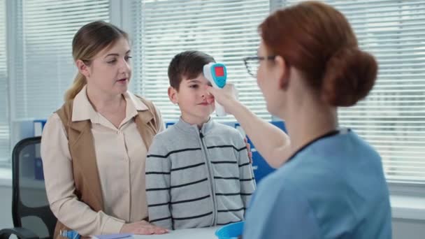 Orvos konzultál a gyerek fiú anyával a kórházban, női terapeuta méri a hőmérséklet a kis beteg érintésmentes hőmérő — Stock videók
