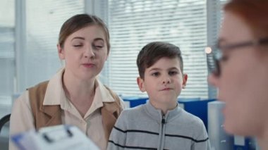 Küçük çocukla gülümseyen anne terapisti yakından ziyaret ediyor, kadın doktor çocuk doktoru hastanedeki not defterine not alıyor.