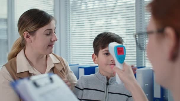 Santé des enfants, pédiatre mesure la température d'un petit patient avec thermomètre sans contact puis prend des notes dans le presse-papiers — Video