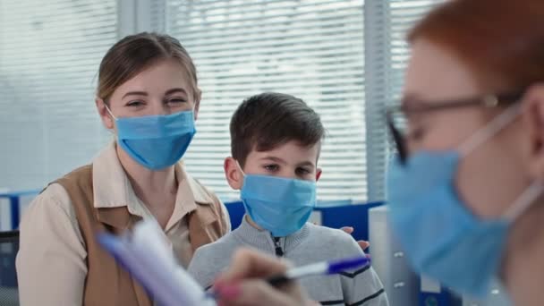 Дети медицинское обслуживание, врач и пациенты в масках во время консультации в больнице, терапевт пишет в буфер обмена — стоковое видео