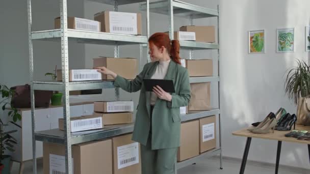 El retrato del pequeño empresario joven con la tableta en las manos comprueba las órdenes de los compradores de la tienda de ropa en línea en el almacén boutique, sonríe y mira la cámara — Vídeos de Stock