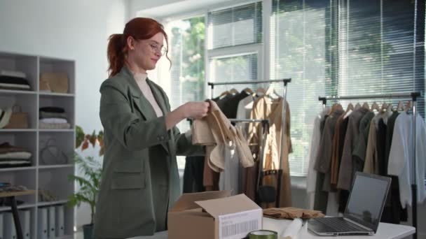 Online kledingwinkel, jonge vrouwelijke ondernemer is het verpakken van goederen aan kopers van een internet winkel voor levering achtergrond van planken in boetiek — Stockvideo