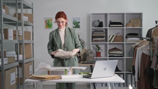 Online-Handel, eine junge Verkäuferin eines Internet-Bekleidungsgeschäfts wickelt ein Paket mit einem Laptop ein, um es im Hintergrund eines Schaufensters an Kunden zu senden — Stockvideo
