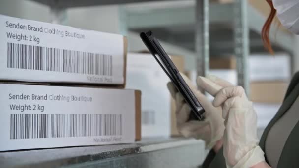 Доставка товара, молодая женщина в перчатках проверяет заказы на отправку клиентам магазина интернет во время работы на складе магазина во время карантина — стоковое видео