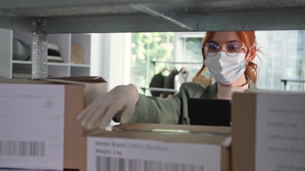 Tıbbi maske takan genç bayan küçük işletme sahibi karantina üzerinde çalışırken çevrimiçi bir mağazanın müşterilerine teslimat ayarlıyor. — Stok video