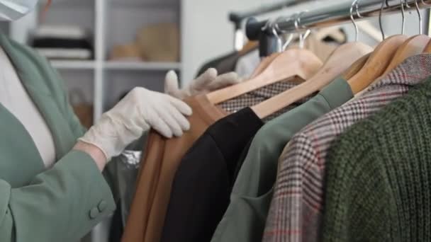 Abertura da loja, jovem mulher vendedor observa precauções de segurança e usa luvas médicas enquanto trabalhava em uma loja de roupas e verifica bens em cabides, close-up — Vídeo de Stock
