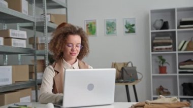 Küçük işletme, gözlüklü güzel bir genç kadın ve bayan meslektaşı butikte bir depoda otururken müşterilere çevrimiçi bir giyim mağazasında mal teslimatı yapıyor.