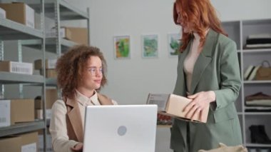Genç bayan iş adamları küçük işletme sahipleri, mağazadaki masada oturan bir internet giyim mağazasının müşterileri için dizüstü bilgisayarda mal teslimatı ayarlıyorlar.