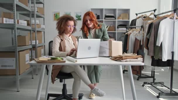 Портрет жінок-бізнесменів, які роблять доставку одягу клієнтам в інтернет-магазині, сидячи за столом з ноутбуком в модному бутіку — стокове відео