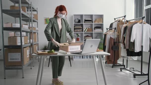 Arbeta på distans, unga småföretagare bär en medicinsk mask och handskar förpackar varor för att leverera beställningar till online shoppare i klädbutik bakgrund hyllor med lådor i en butik — Stockvideo