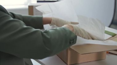 Karantinada küçük bir işletme, tıbbi eldivenli genç bayan satış elemanı bir iç giyim mağazasının müşterilerine teslim edilecek eşyaları paketliyor, yakın plan.
