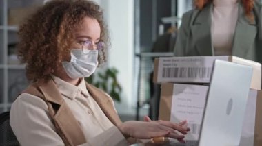 Bırakma işi, yüzüne tıbbi maske takan genç bayan girişimci, teslimat kutularını elinde tutan meslektaşı ile çevrimiçi mağazadaki müşterilere sipariş veriyor.