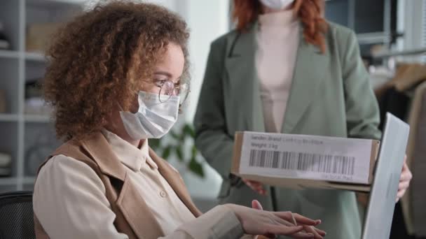Küçük işletme, gözlüklü, yüzünde tıbbi maske olan genç bir kadın elbise deposundaki bilgisayardan sipariş formu dolduruyor. — Stok video