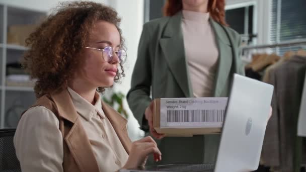 Modern ung kvinna använder modern teknik och säljer varor i en webbutik, ordna leveranser för en kund som sitter i ett klädlager — Stockvideo